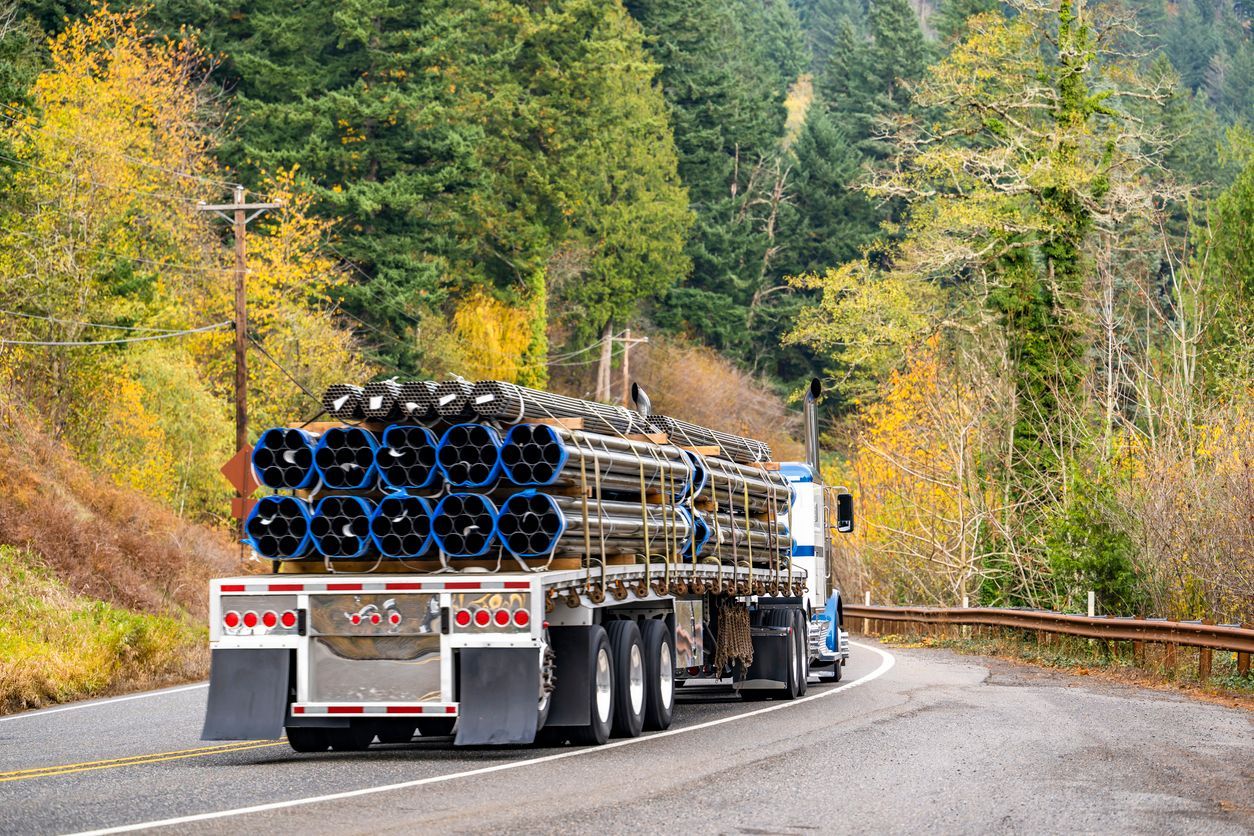 Truck hauling a load of blue and black pipes on a winding road through a forest.