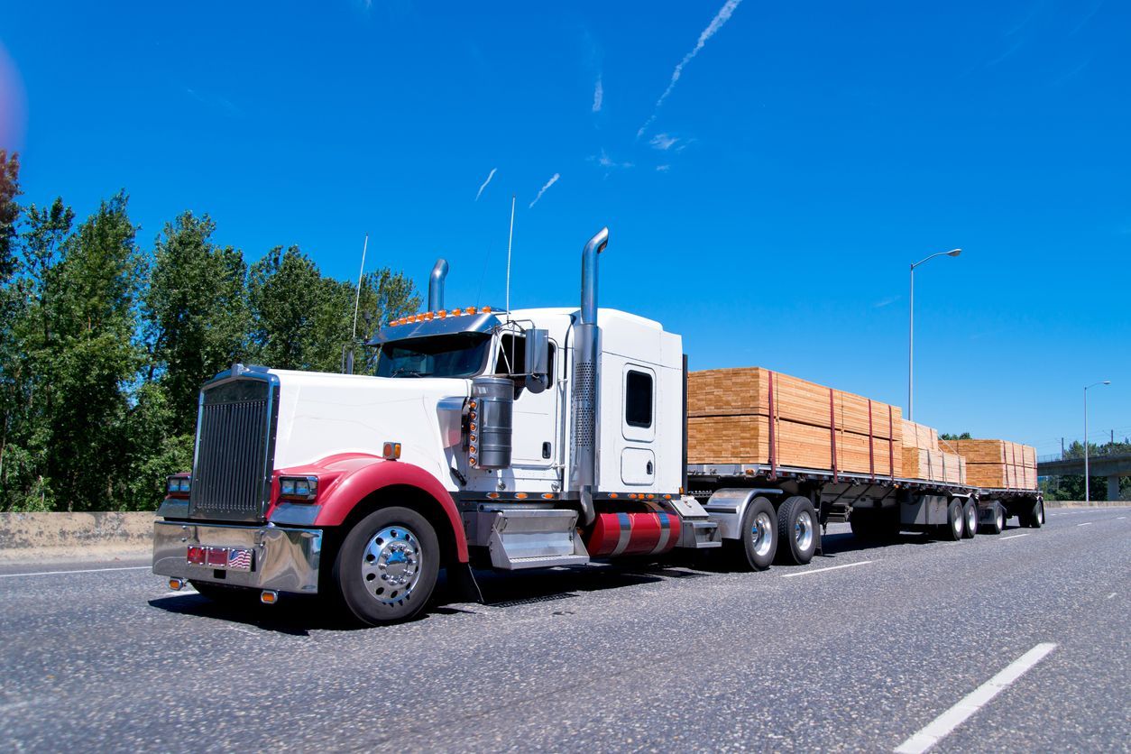 White and red semi-truck hauling lumber on a sunny road.