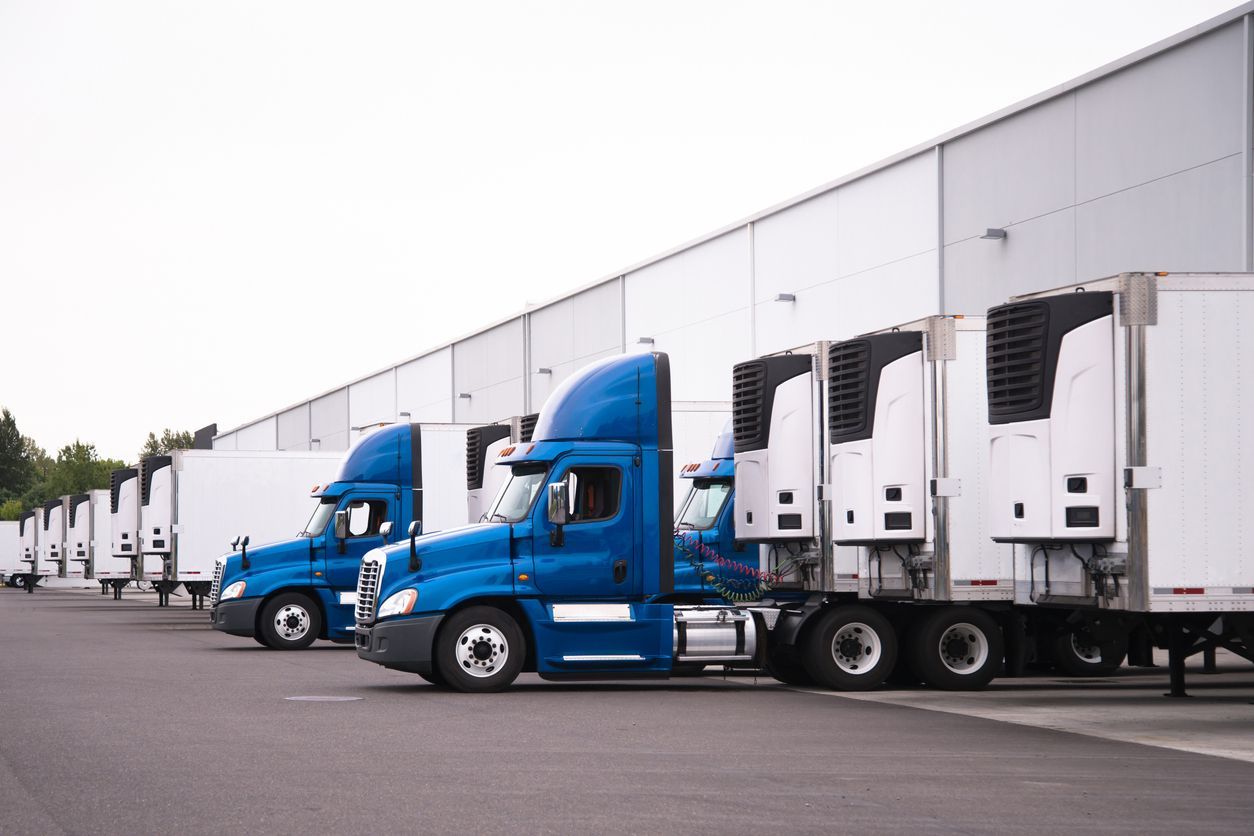 Blue semi-trucks parked at a white loading dock, trailers aligned.