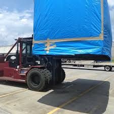 Forklift loading a blue shipping container onto a train car at a port.