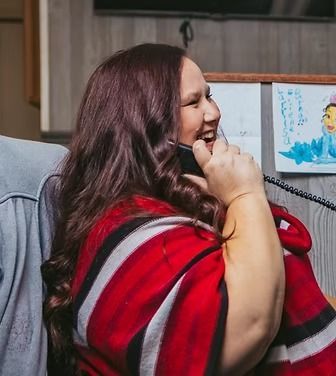 Woman with long, wavy auburn hair laughs while on the phone, wearing a red and white striped shawl.