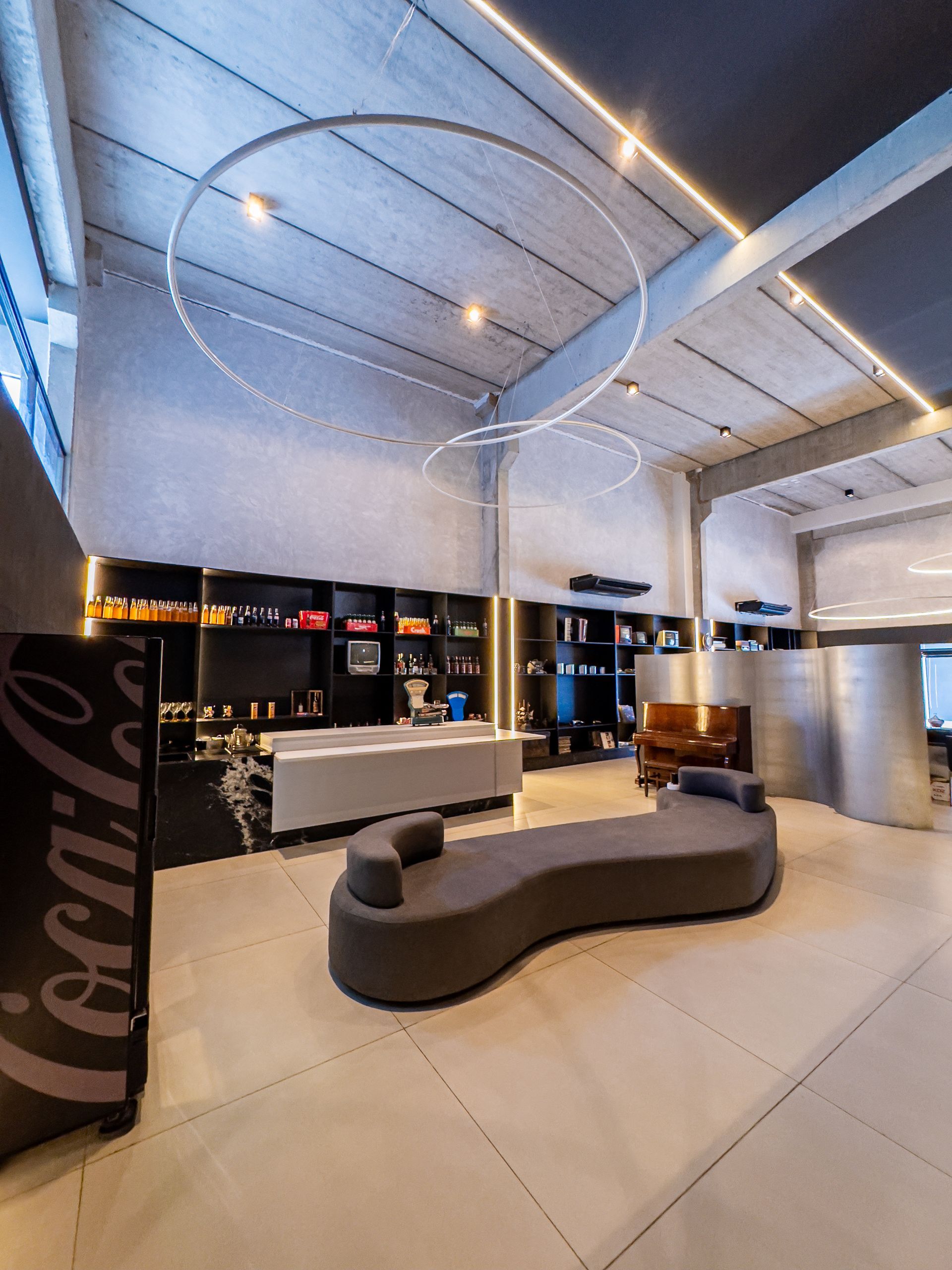 Interior moderno com decoração em tons de cinza e preto, sofá, área de bar, luminárias circulares e placa da Coca-Cola.