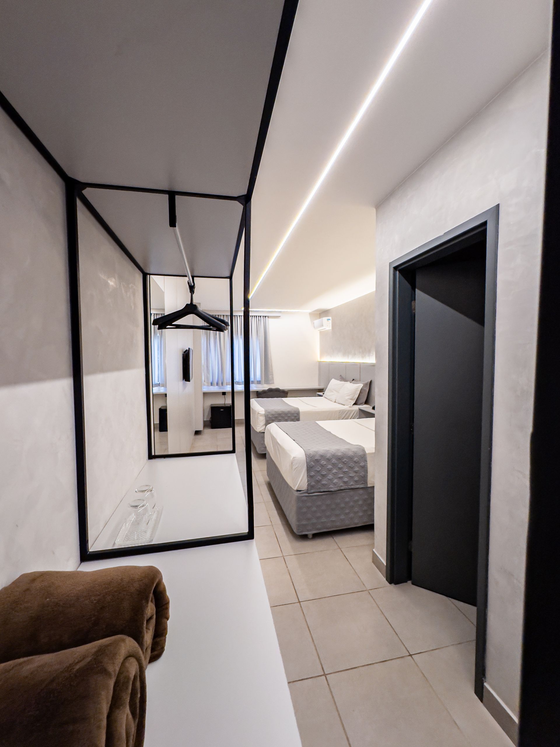 Corredor de quarto de hotel moderno com guarda-roupa, camas e porta escura.