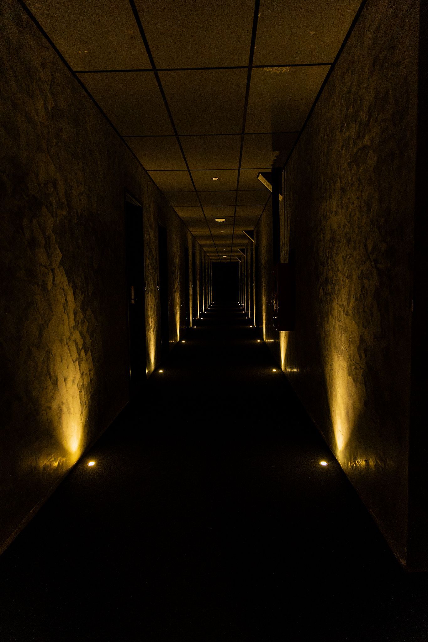 Um corredor escuro e comprido com iluminação embutida e paredes iluminadas.