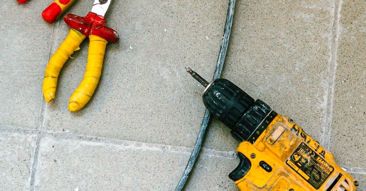 A drill and pliers are sitting on a tiled floor.