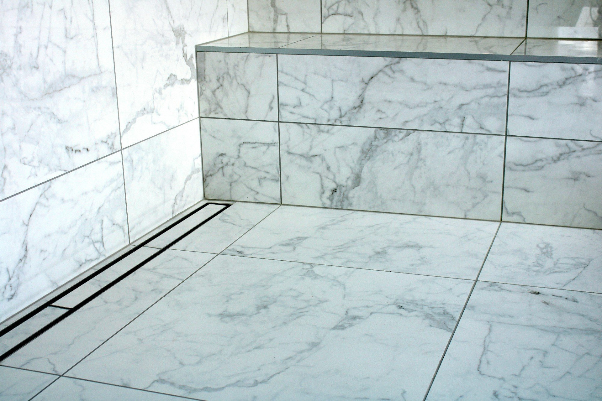 A bathroom with marble tiles and a drain in the floor.