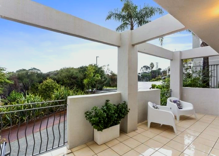 A balcony with white chairs and a potted plant.
