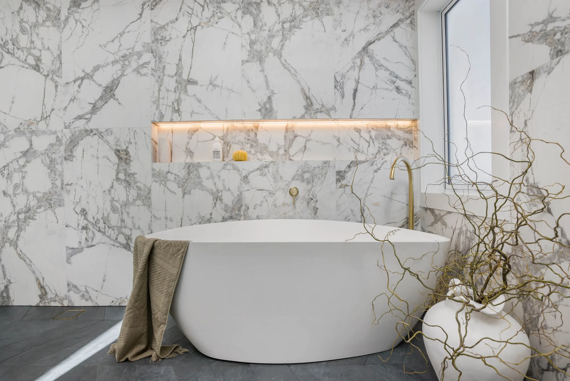 Luxurious bathroom with marble walls, a freestanding white tub, and decorative branches.