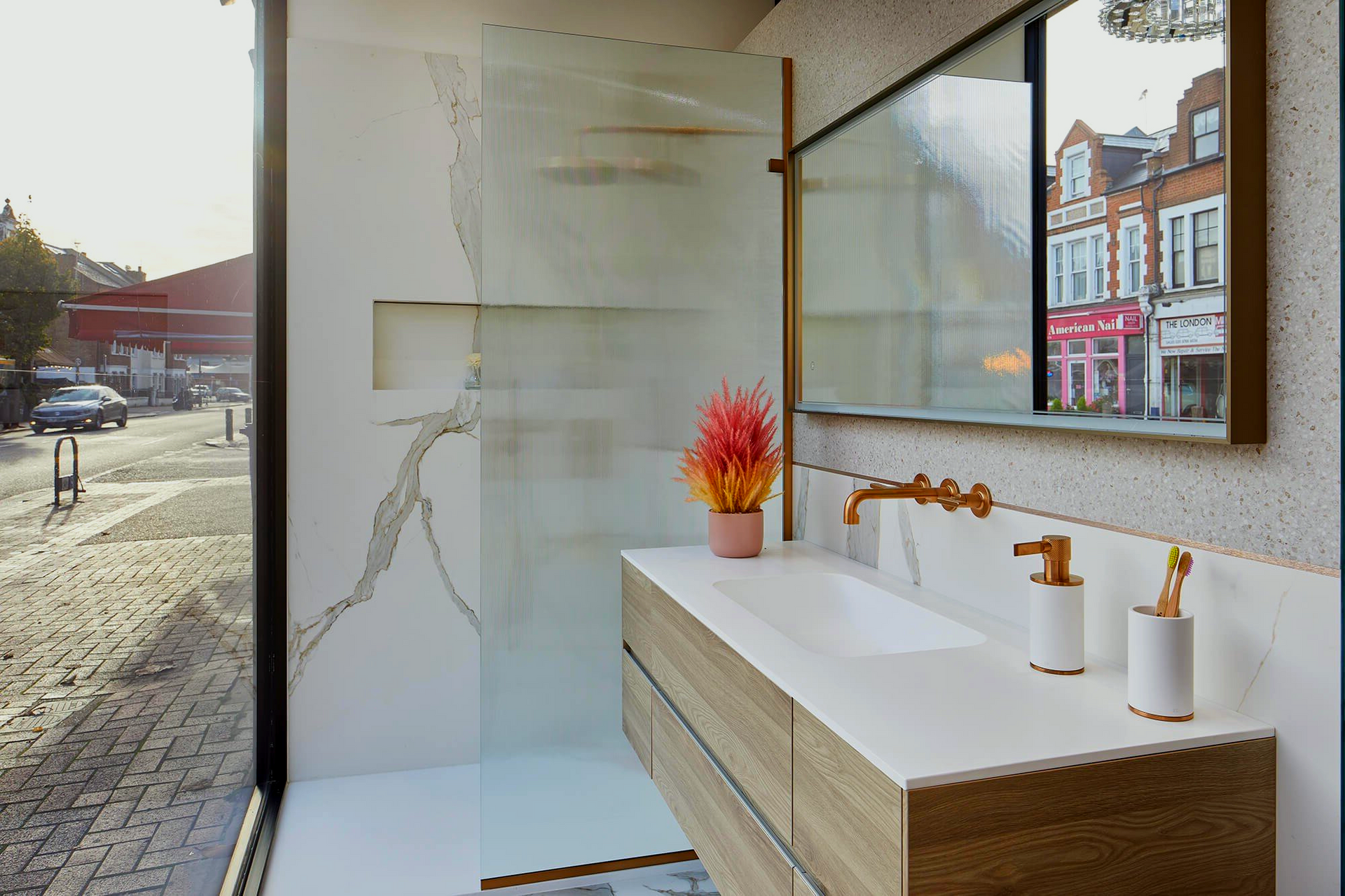 A bathroom with two sinks, a mirror and a walk in shower next to a street.