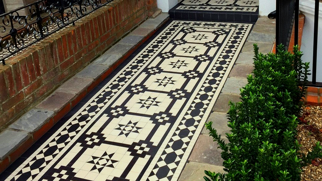 Black and white tiles on the sidewalk next to a brick wall.
