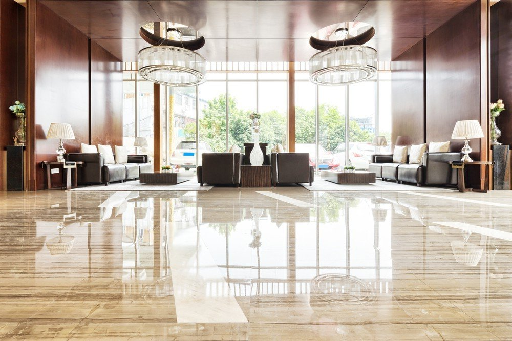 Hotel lobby with polished marble commercial tiling, seating, and large windows overlooking greenery.