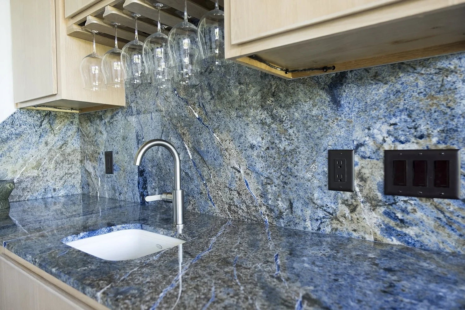 Blue granite countertop with a sink, faucet, and power outlets. Wine glasses hang from a rack.