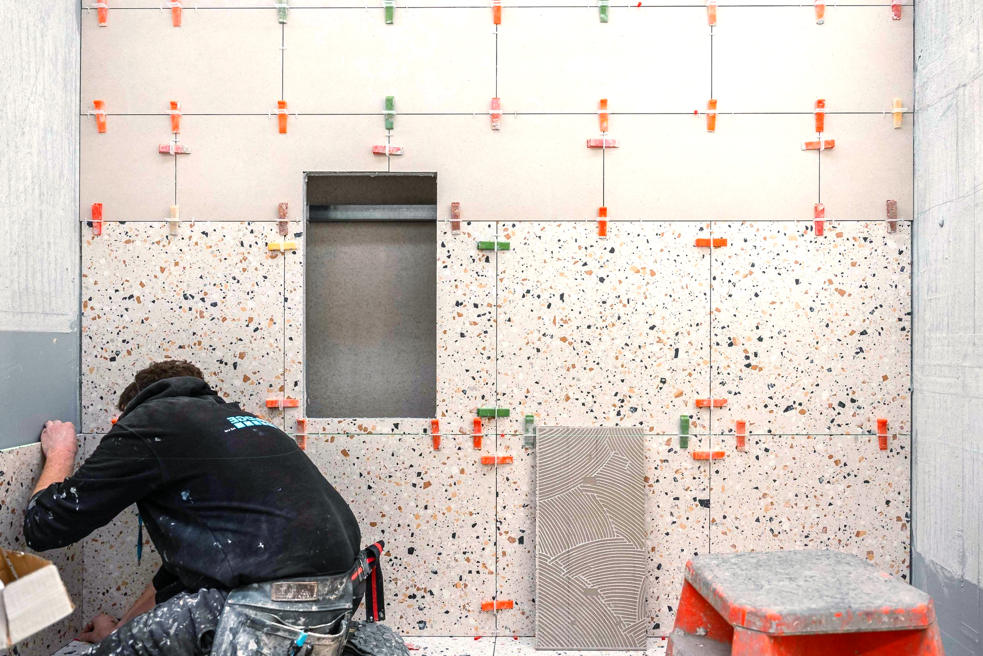 A man is working on a tiled wall in a bathroom.
