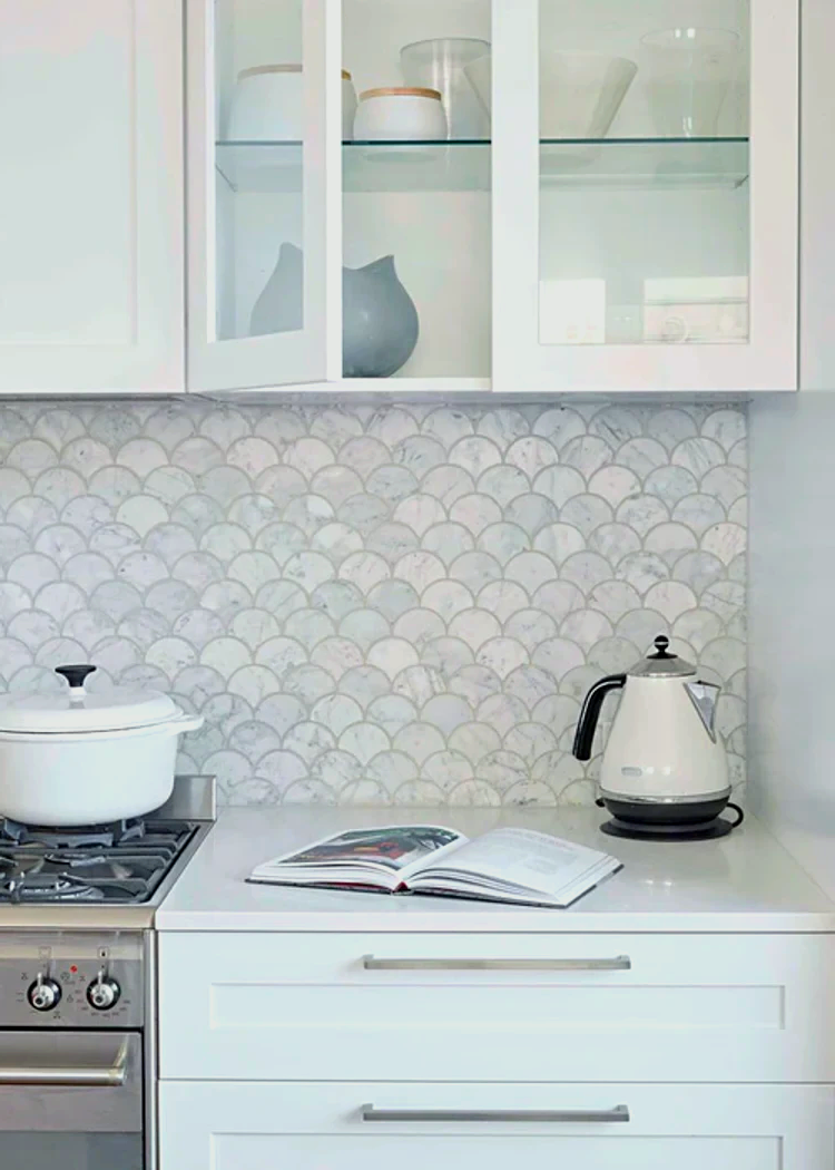 A kitchen with white cabinets, a stove, a kettle, and a book on the counter.