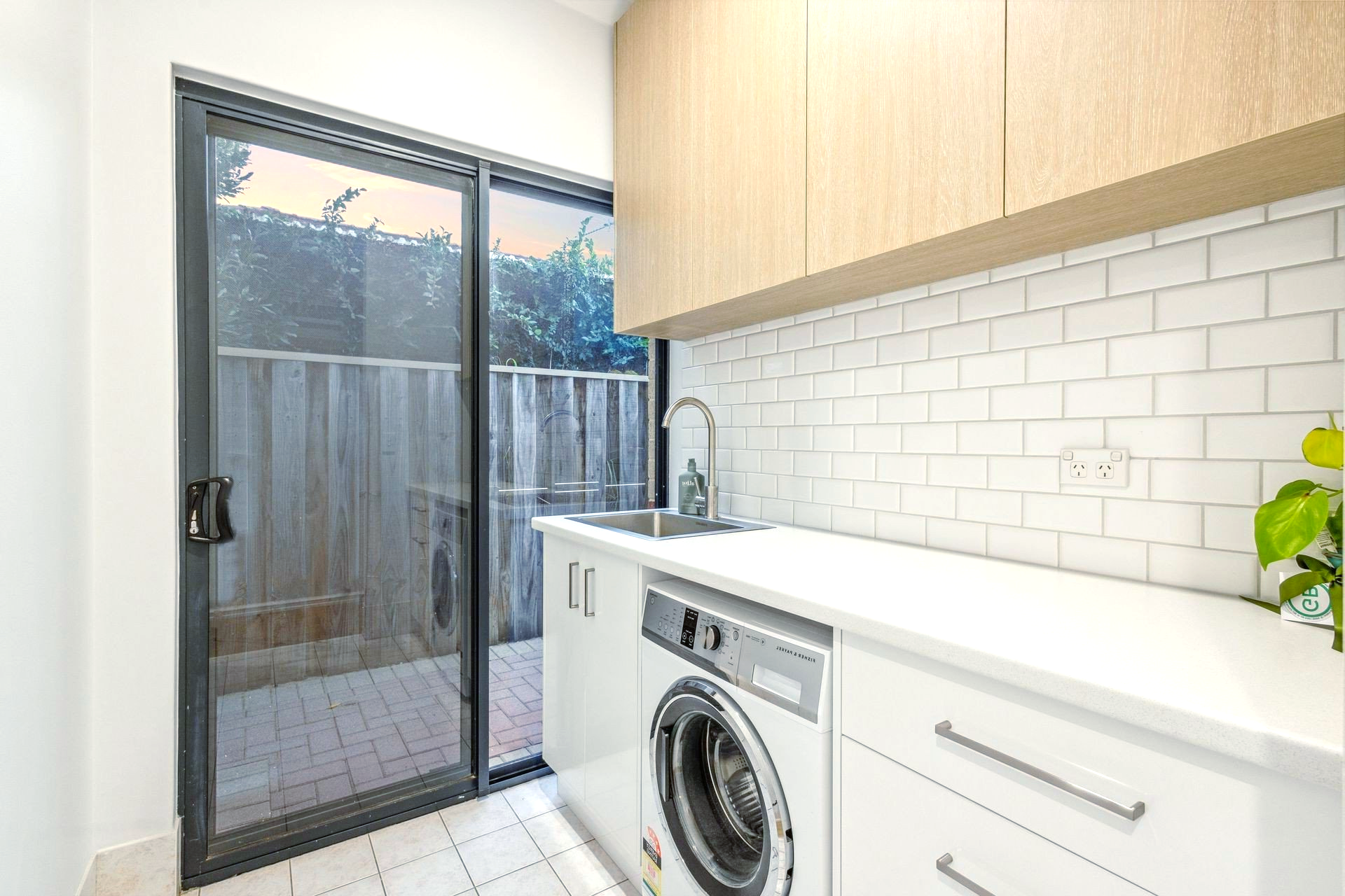 A laundry room with a washing machine, sink and sliding glass door.
