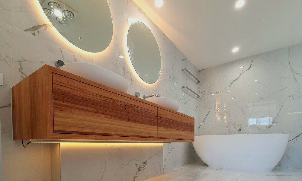 Modern bathroom with wooden vanity, two round backlit mirrors, and a freestanding tub.