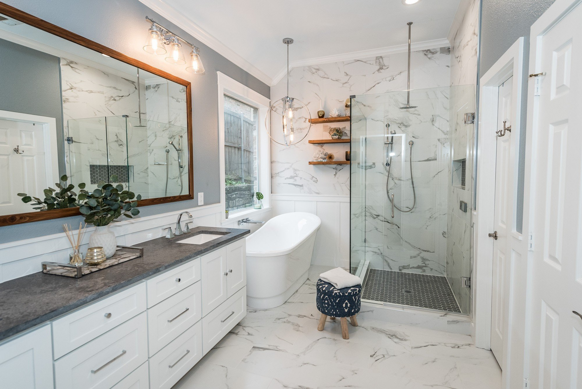 Modern bathroom with white marble, large mirror, freestanding tub, and glass shower.