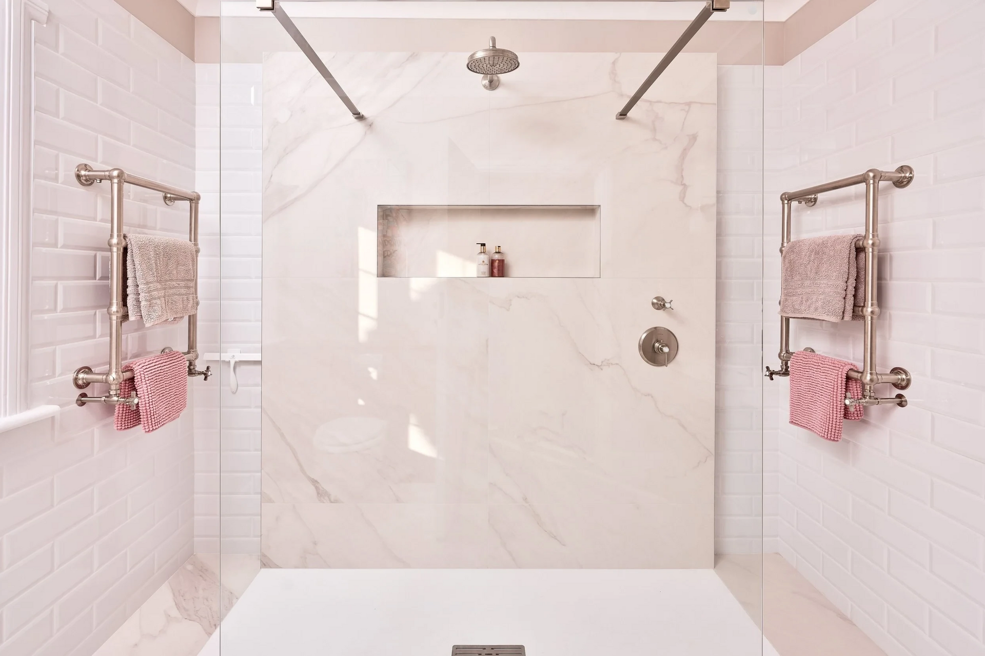 Bright, modern walk-in shower with marble-look wall. Towel warmers, recessed shelf, and glass enclosure.