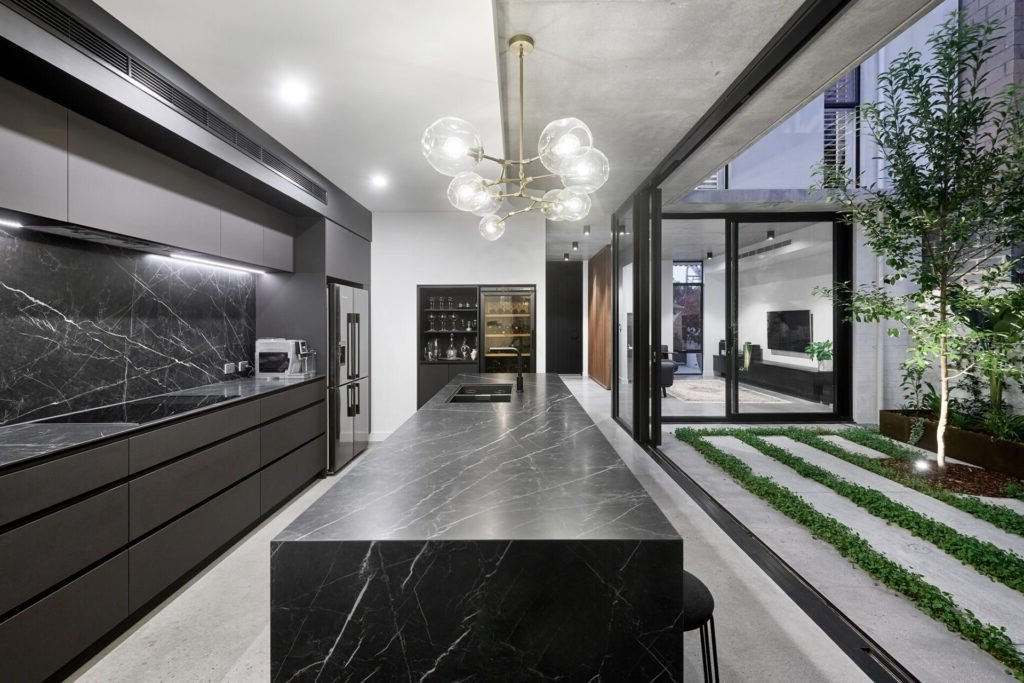 Modern kitchen with black marble counters, sleek black cabinets, and an outdoor patio.