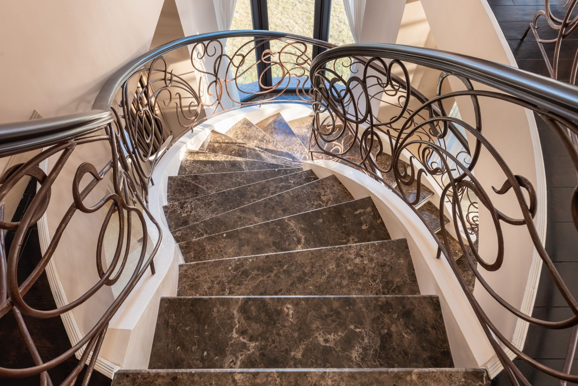 Elegant, curved staircase with marble steps and ornate wrought-iron railing.