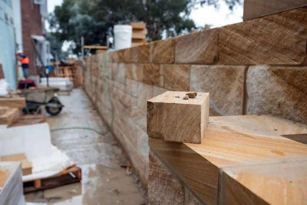 Sandstone retaining wall under construction with a single brick in focus.