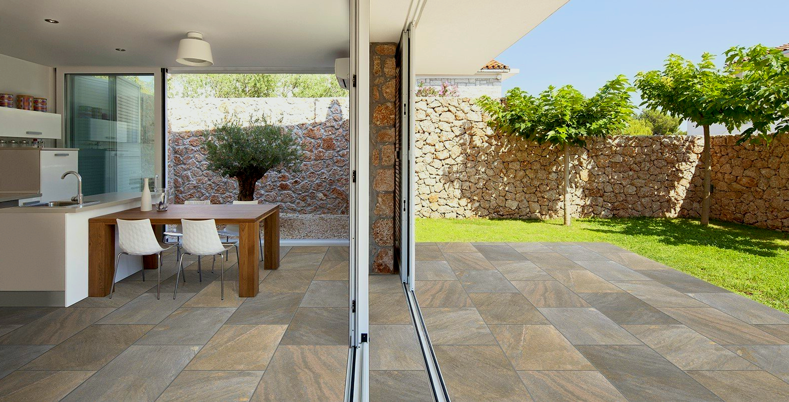Patio with stone flooring, dining table inside, sliding glass doors, grassy yard.