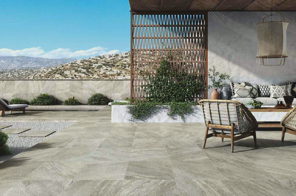 Patio with wicker furniture, plants, and mountain views, under a blue sky.