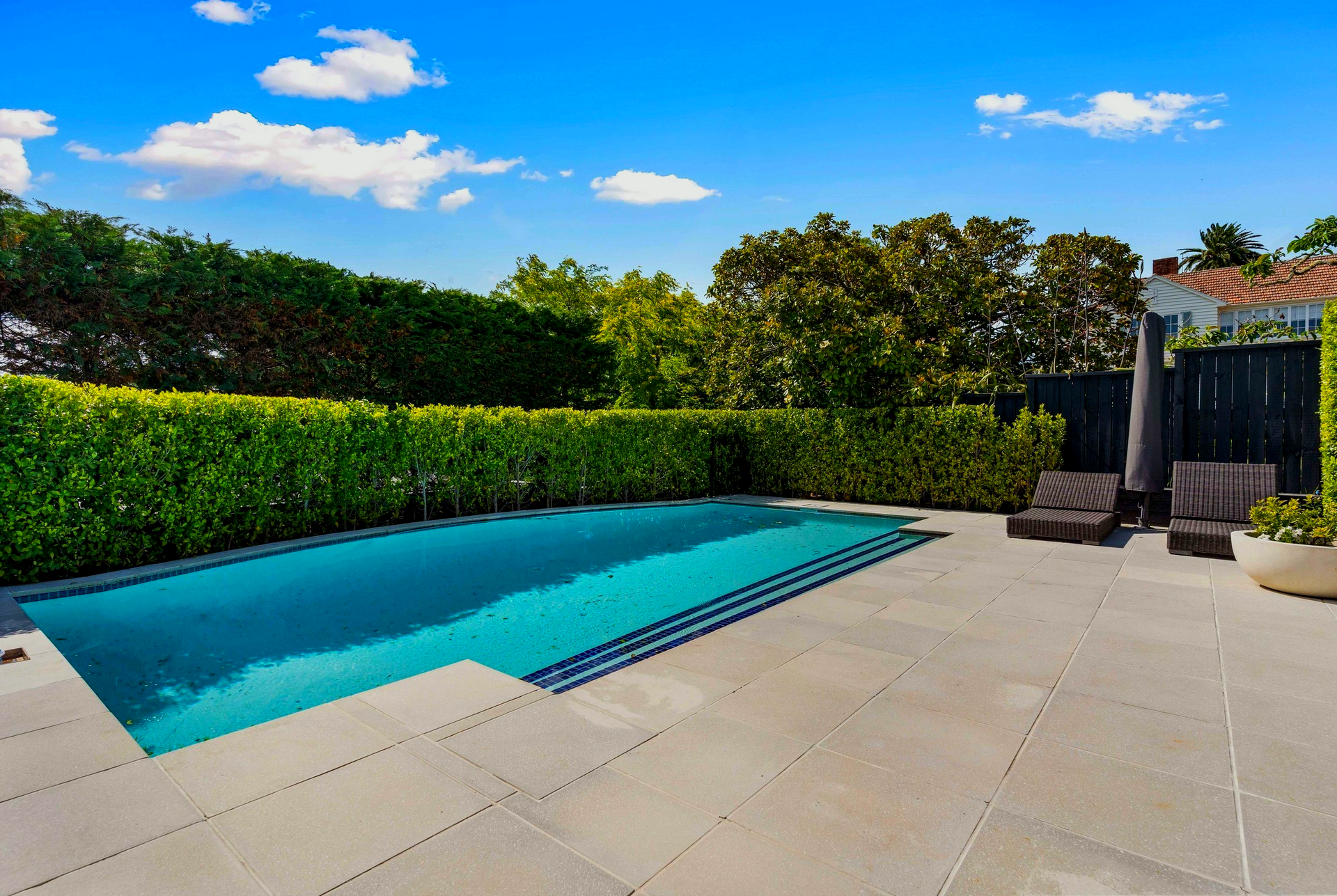 A large swimming pool is surrounded by a hedge and chairs.