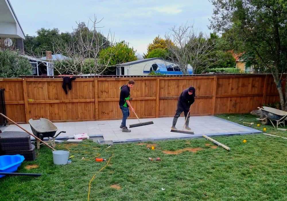 Two men are working on a concrete patio in a backyard.