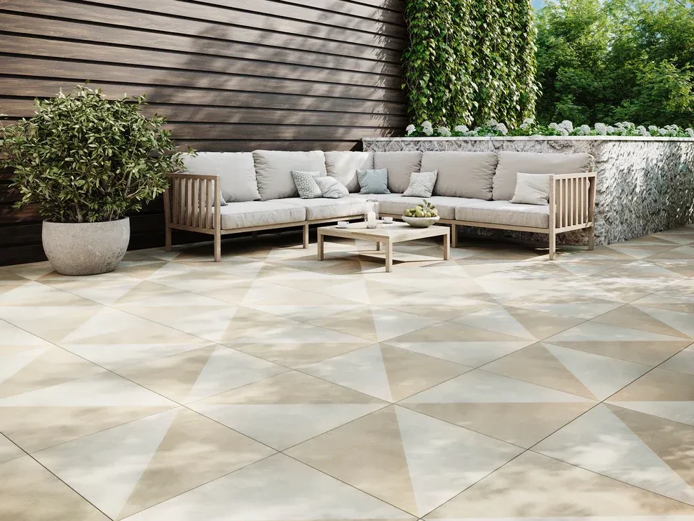 Outdoor patio with geometric tile, sectional sofa, and coffee table; wooden wall and greenery.