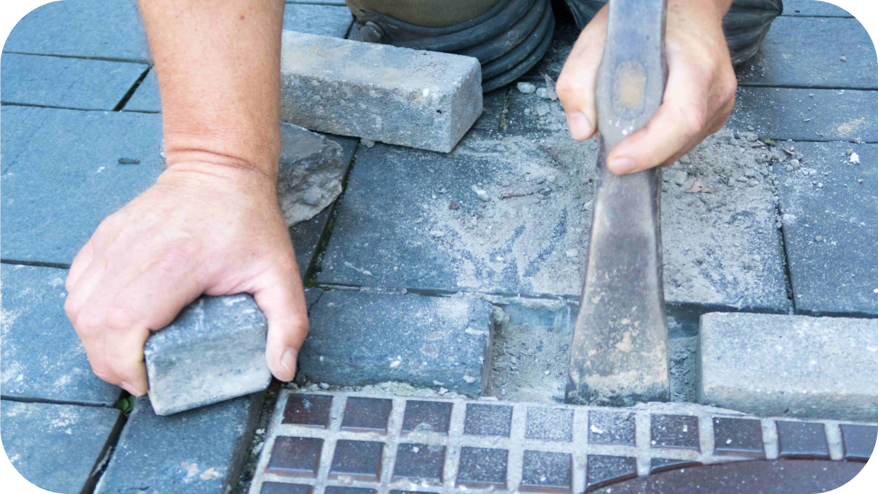 Person chiseling and fitting a paving stone next to a drain.