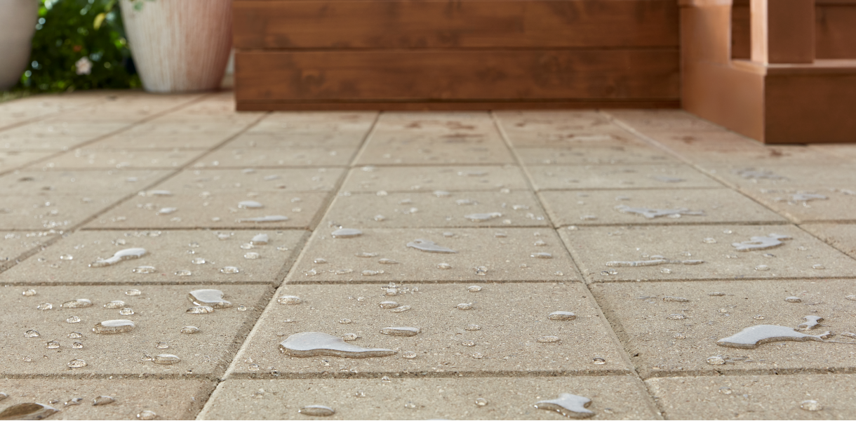 Wet stone tiles on a patio with blurred background of pots, wooden planks, and steps.