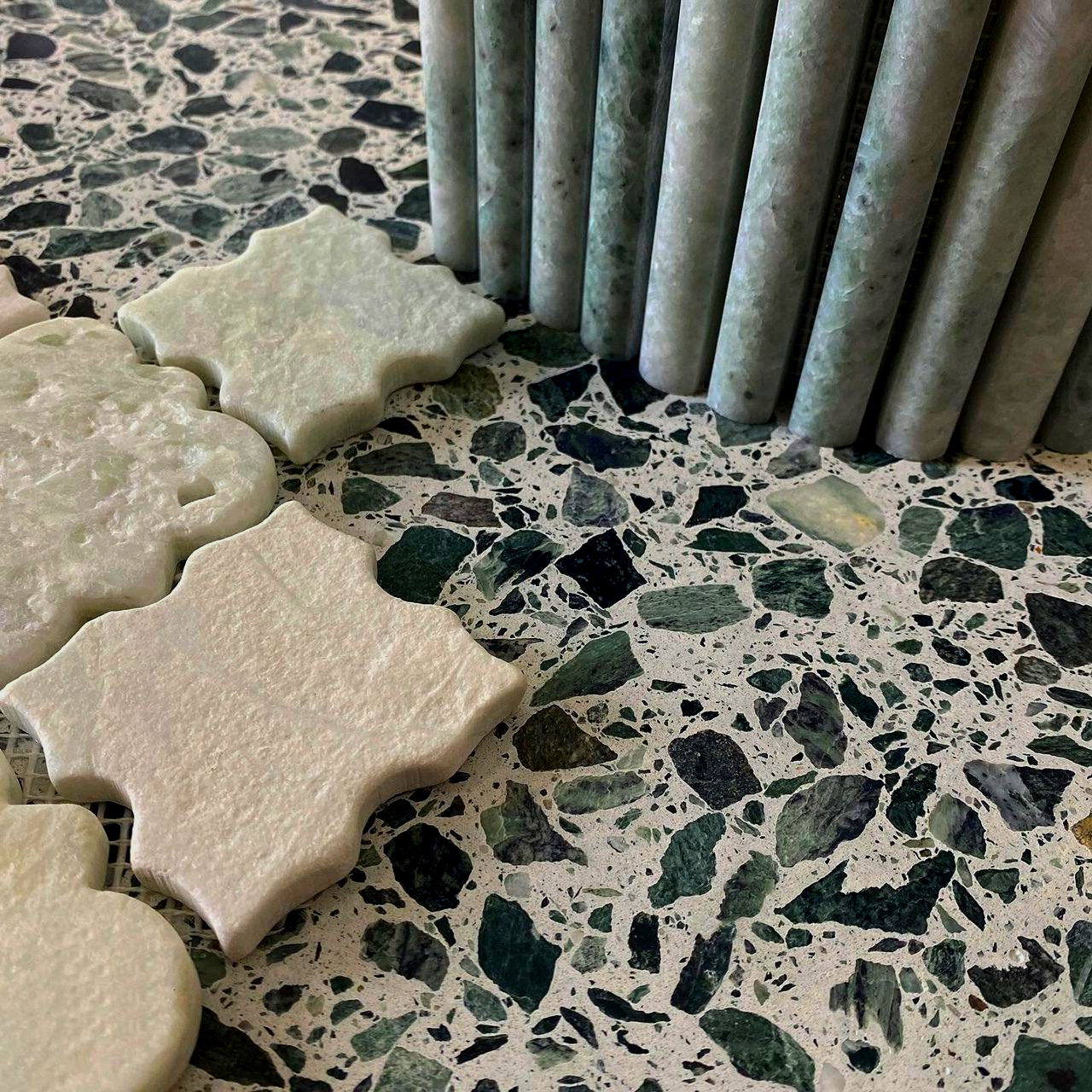 Close-up of tiles: terrazzo flooring with green accents; flower-shaped light tiles and vertical cylindrical tiles in shades of green.