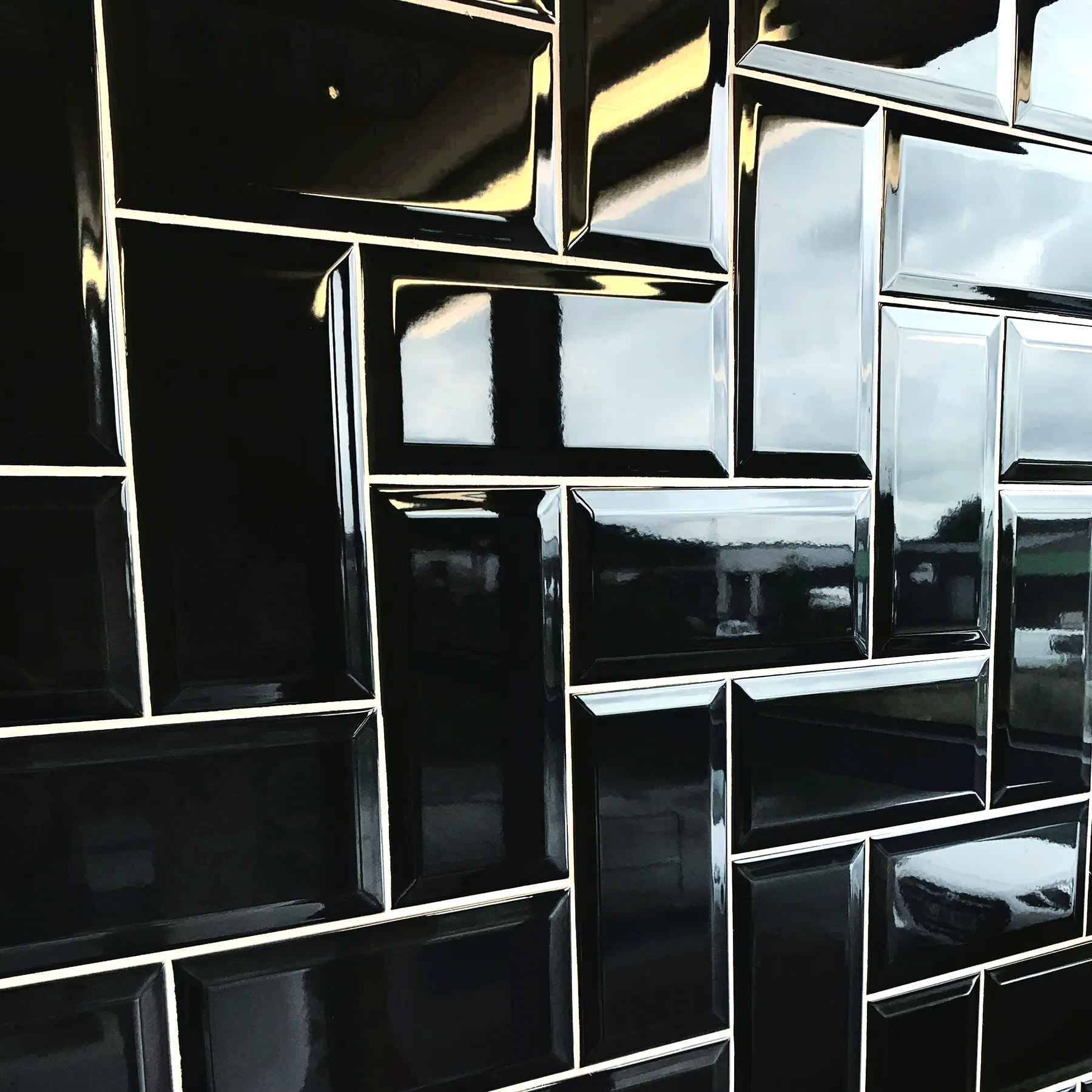 A wall of black tiles reflecting a car parked in the background.