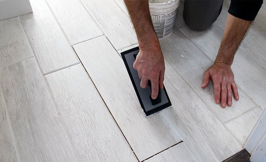 A man is kneeling on the floor using a trowel.