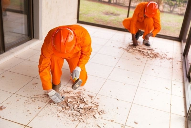 Two men in orange jumpsuits are working on a tiled floor.