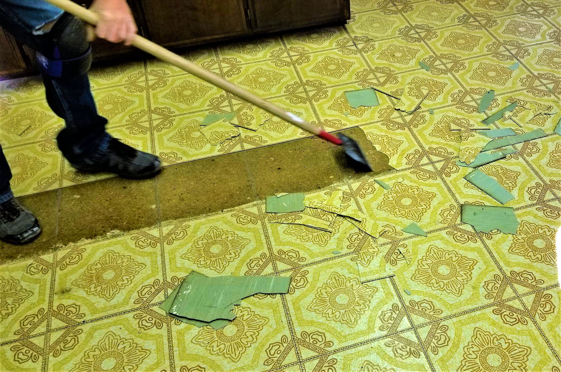 A person is removing tiles from a tiled floor with a shovel.