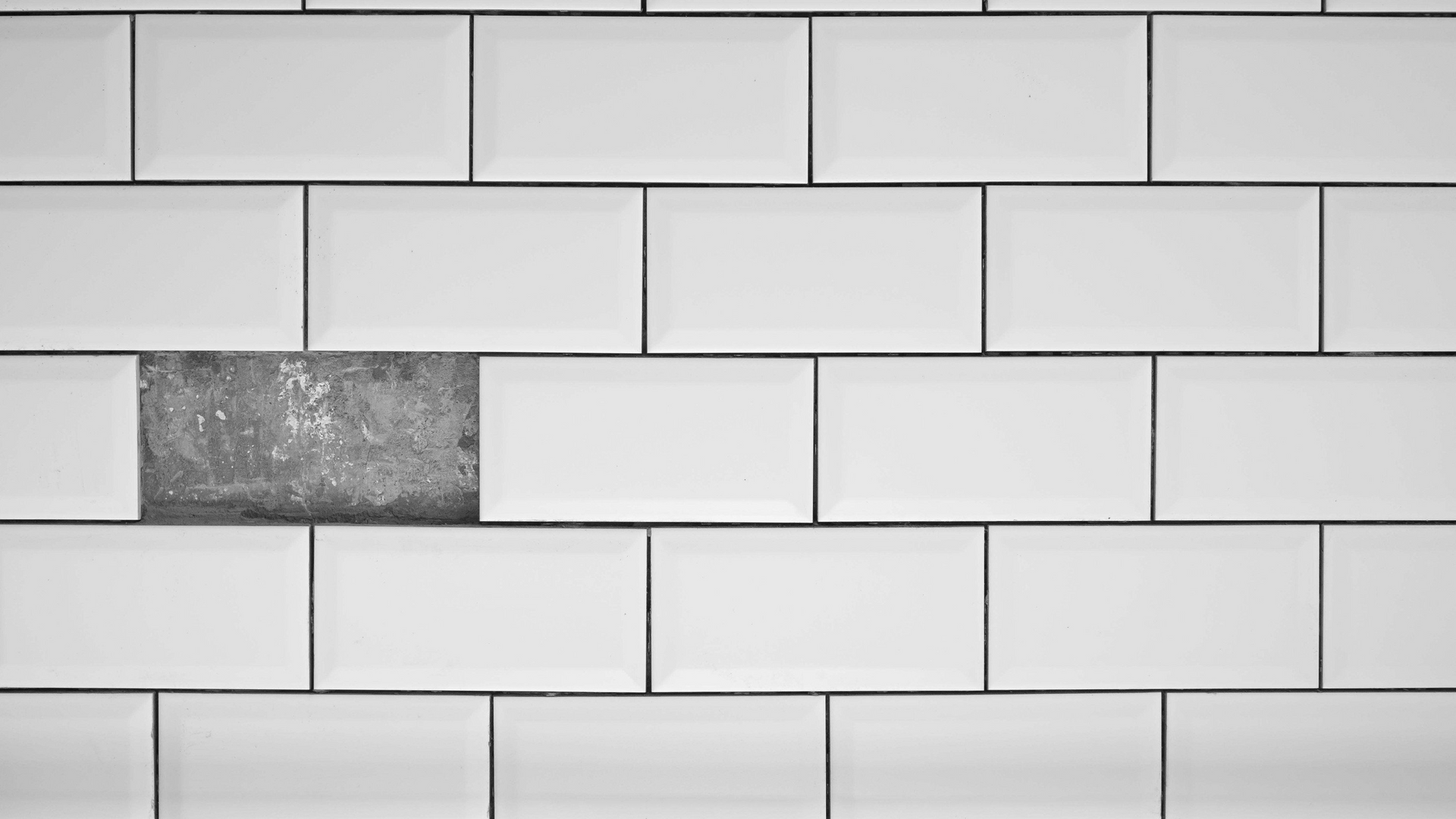 A close up of a white tile wall with a missing tile in the middle.