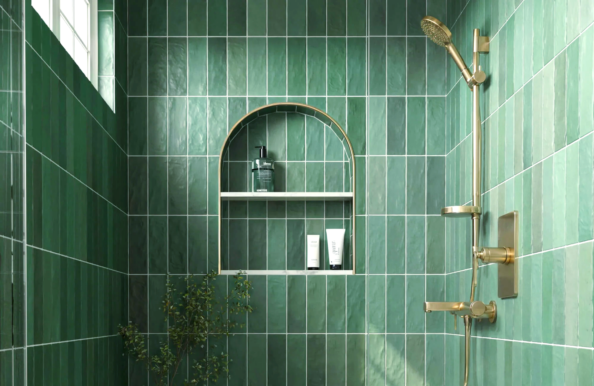 A bathroom with green tiles and a gold shower head.