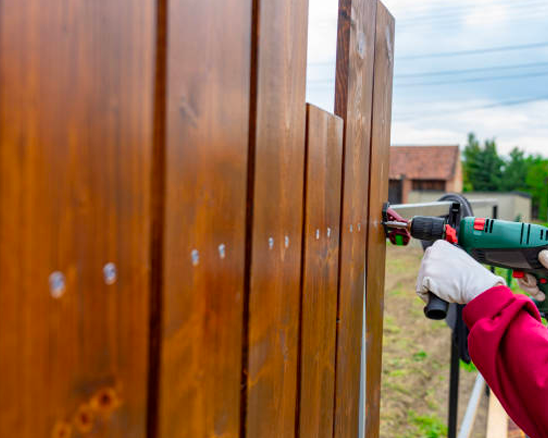 A person is using a drill to install a wooden fence.