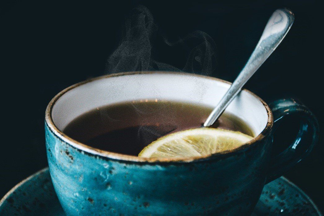 A cup of tea with a spoon and a slice of lemon on a saucer.