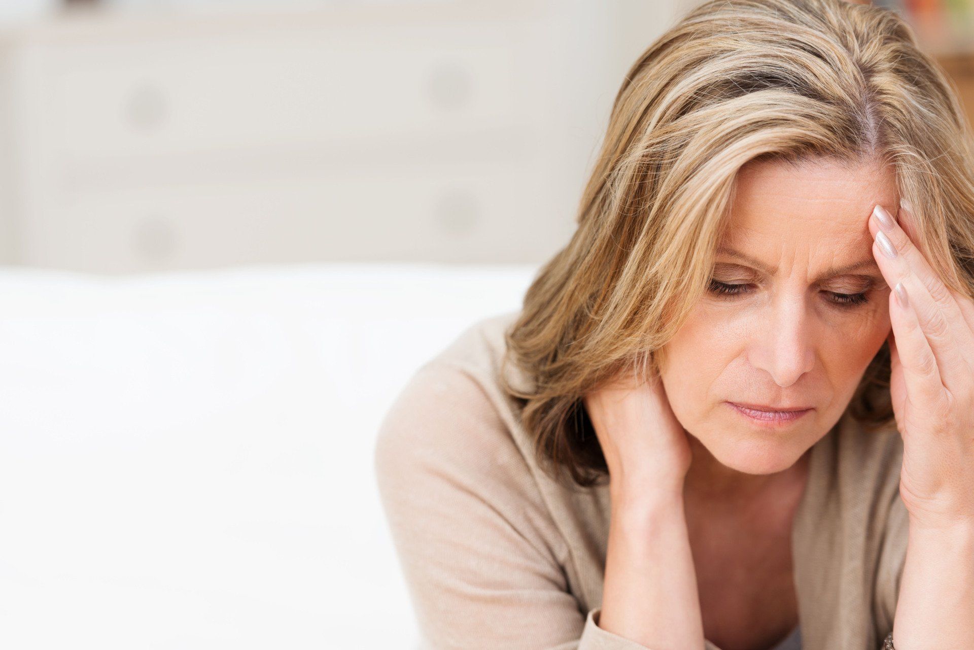 A woman is sitting on a couch with her head in her hands.