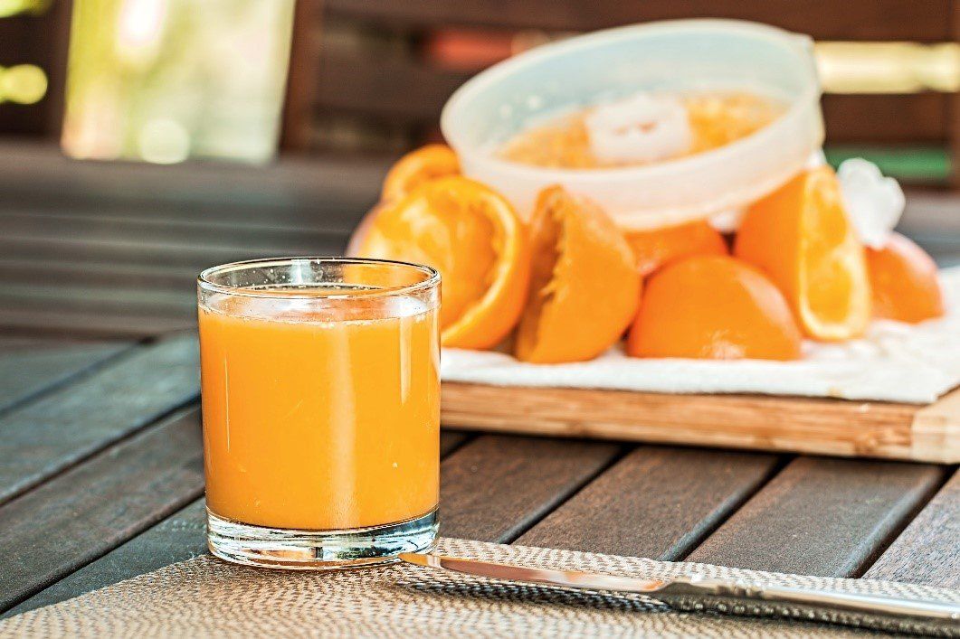 A glass of orange juice is sitting on a wooden table next to oranges.