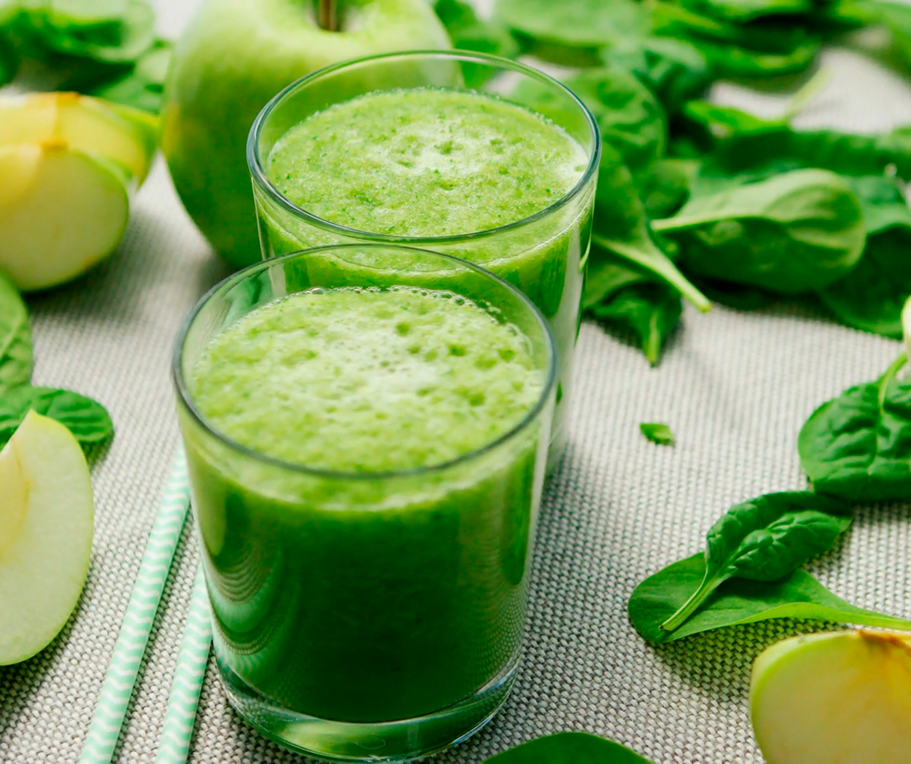 Two glasses of green smoothie with apples and spinach on a table.