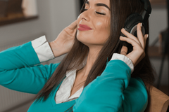 A woman wearing headphones is listening to music with her eyes closed.