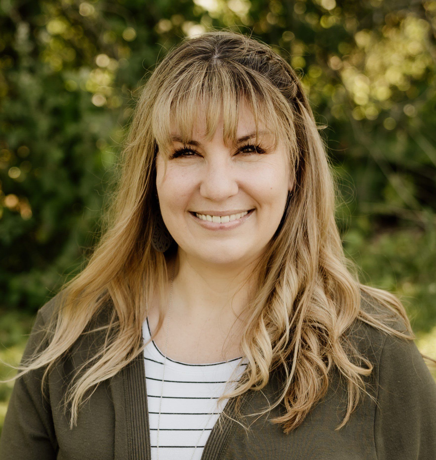 A woman in a green jacket and striped shirt is smiling for the camera.