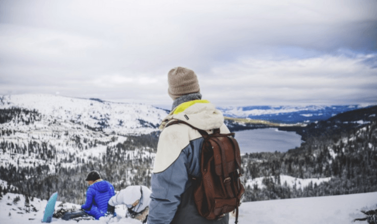 A man with a backpack is standing on top of a snow covered mountain.