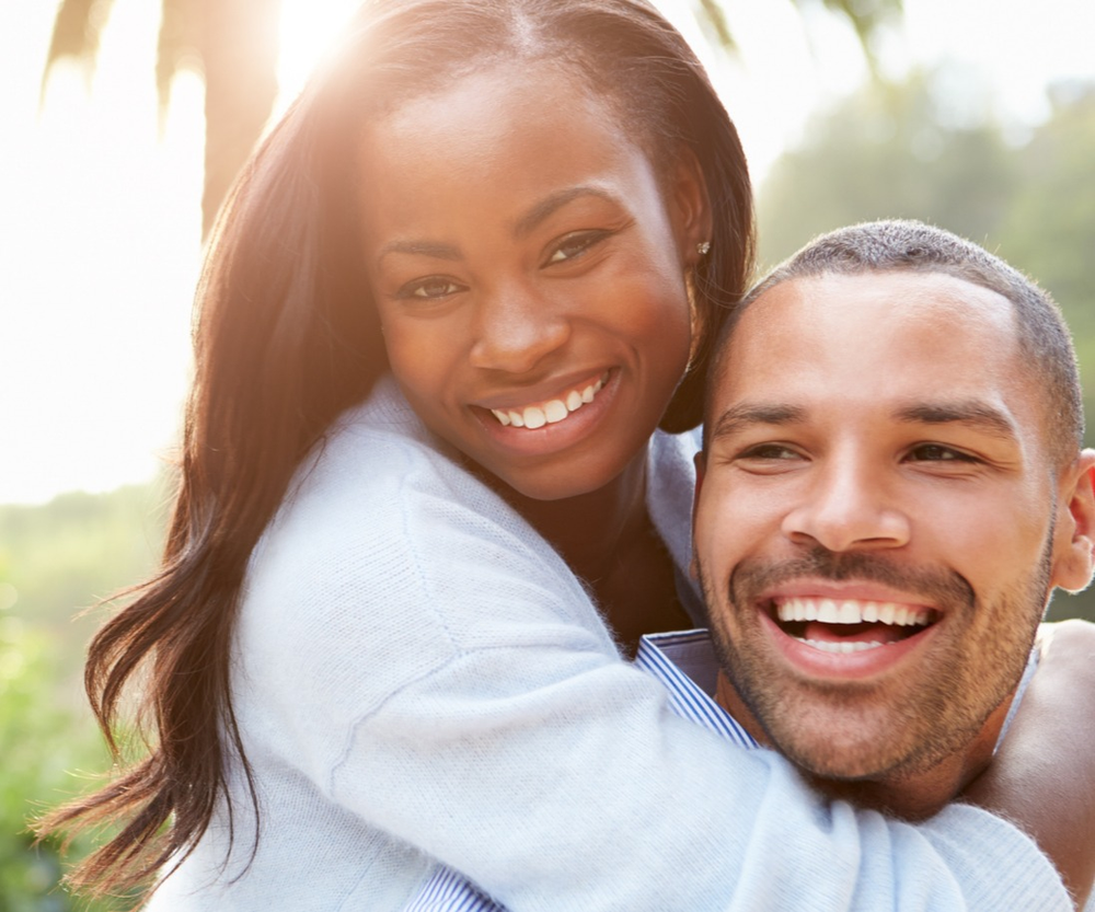 A man is giving a woman a piggyback ride and they are smiling