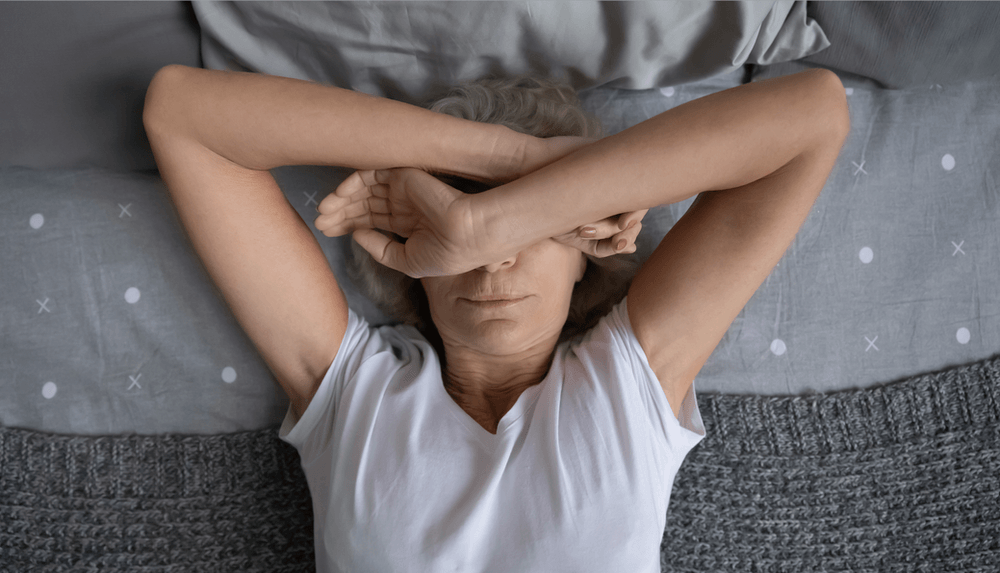 A woman is laying on a bed with her hands covering her eyes.