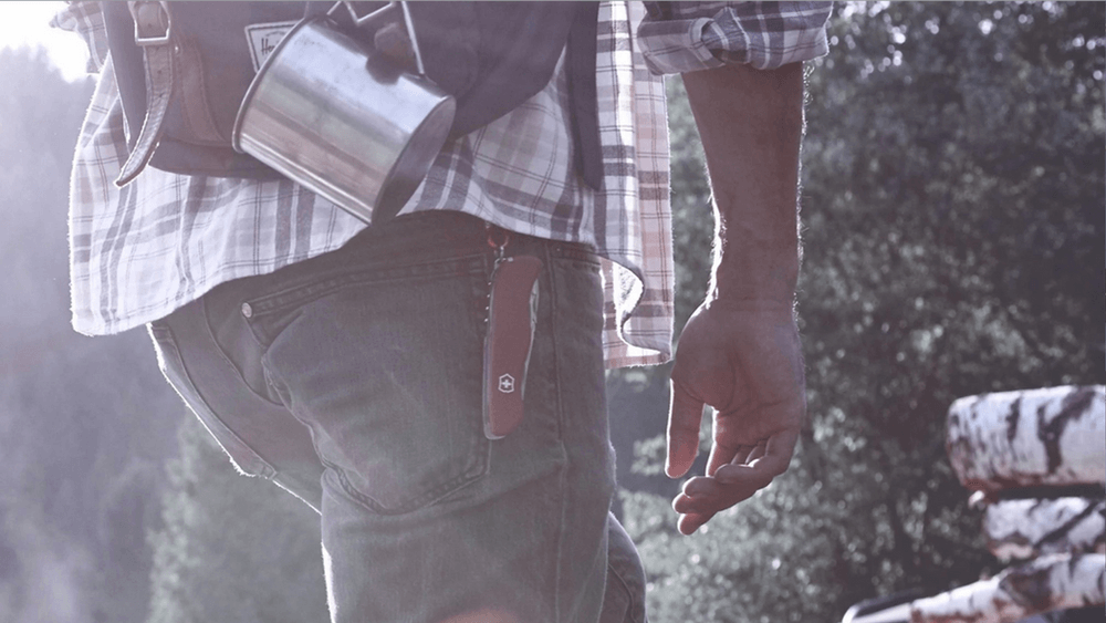 A man is walking with a backpack and a cup in his pocket.